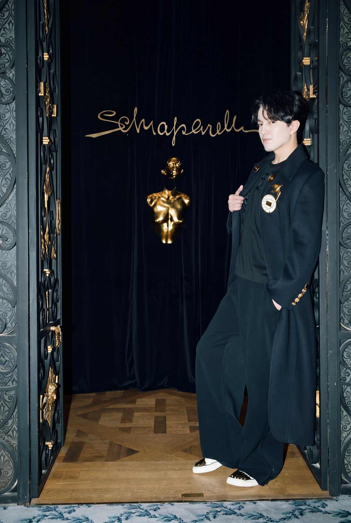 Dimash at the Schiaparelli atelier doorway, gold sculpture and signature visible